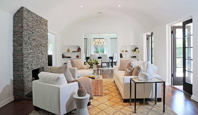 Living room with arched ceiling, a stone fireplace, black French doors, wood floors, a Moroccan style rug with a white sofa and two matching armchairs with neutral accent pillows