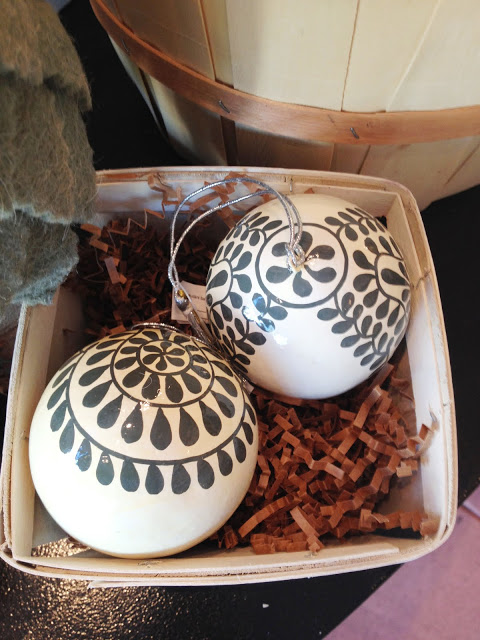 Two Christmas ornaments sitting in brown paper packing material in a white box 