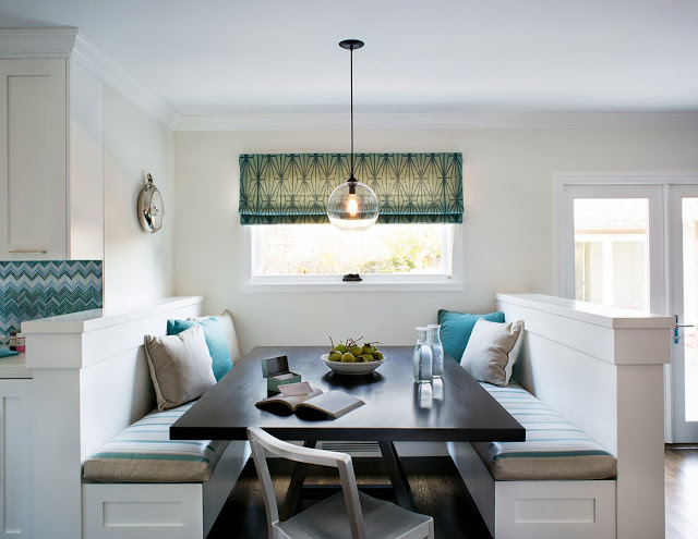 Breakfast nook with built in bench seating with blue and taupe accent pillows, a pendant light and roman shades