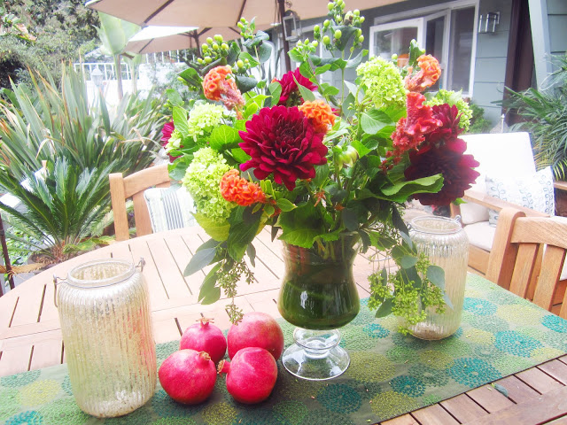 Flower arrangement with dahlia, cockscomb, green coffee beans, seeded eucalyptus, baby hydrangeas and tea leaves on a table in a backyard