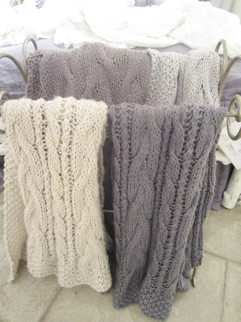 Close up of Pom Pom's chunky knit throws in light purple, grey, white and cream.