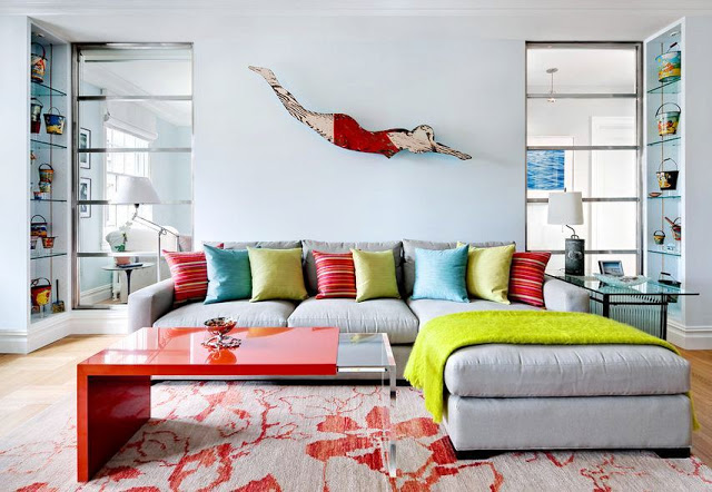 beach themed living room with folk art of a woman in a vintage swim costume diving on the wall, gray and red printed rug, gray sectional sofa with striped, turquoise and green accent pillows
