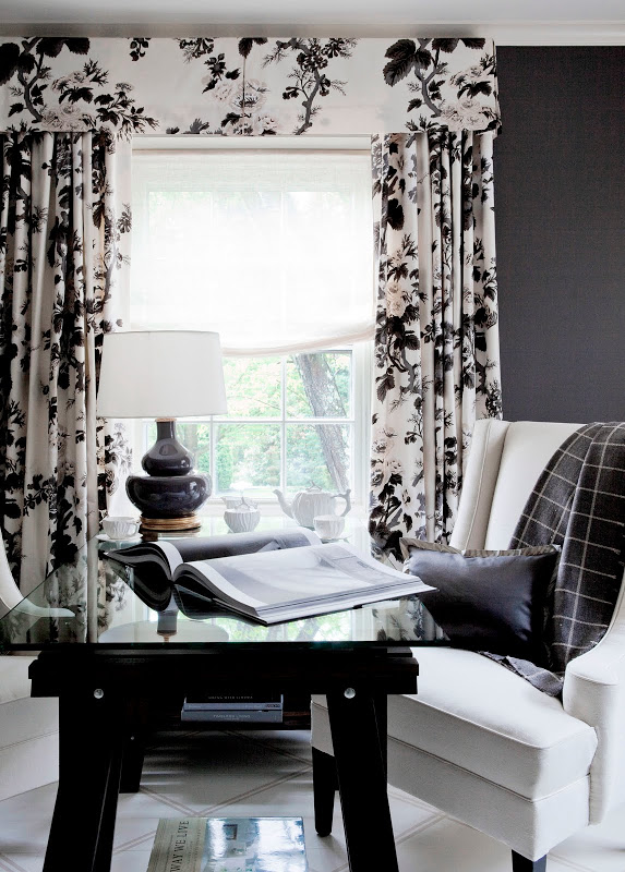 Bedroom with a black writing desk, white armchair with a grey throw, gray walls and chintz curtains