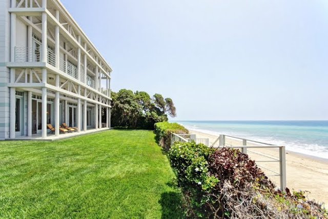 exterior view of a malibu beach front property with lawn and stairs leading directly to the beach