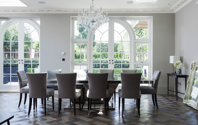 Dining room in a suburban London home with carved crown moulding, ceiling medallions, parquet wood floors, crystal chandelier and arched french doors overlooking a manicured backyard