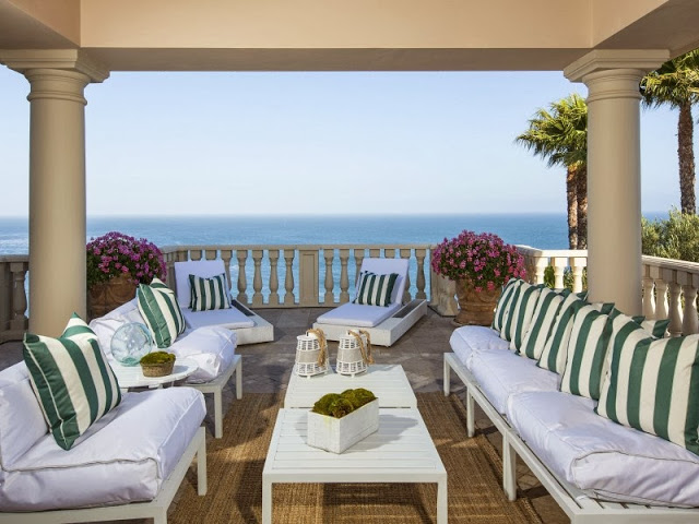 Outdoor patio with green and white stripe pillows, white outdoor chairs and an ocean view