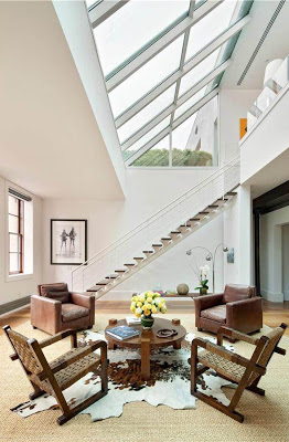 Den in a NYC apartment with a massive skylight, animal hide rug, two matching armchairs and tow matching rocking chairs with woven backs around a small round wood table