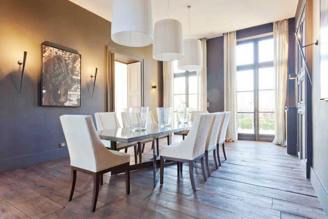dining room with three pendant lights, torch lamps, two toned walls (gold and brown), wood floors, french doors with floor length curtains, a long table with white chairs