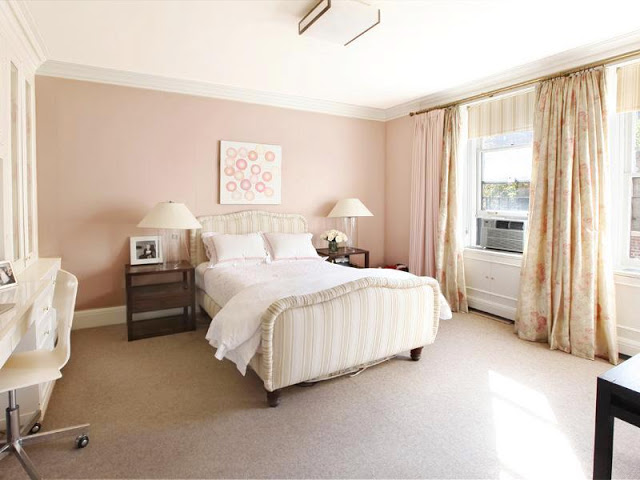 Bedroom with striped upholstered head and footboard, two wooden night stands, pale pink walls, carpeted floor and floor length, floral print curtains