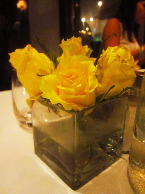 yellow roses in a square vase on a dining room table