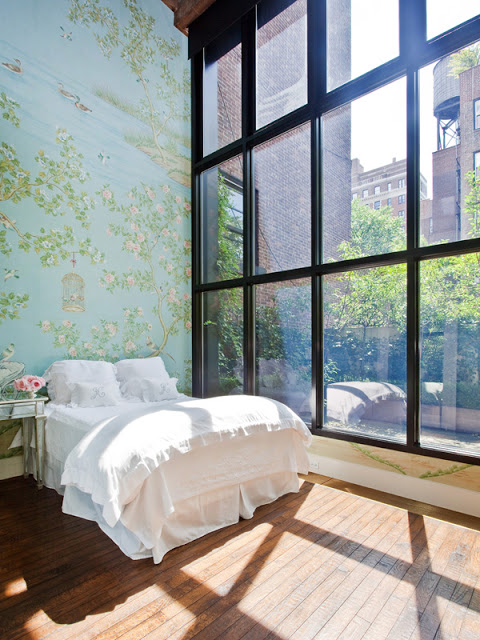 bedroom with iron framed floor to ceiling windows with a view, a large wall with floral wallpaper, a wood floor and a simple white bed