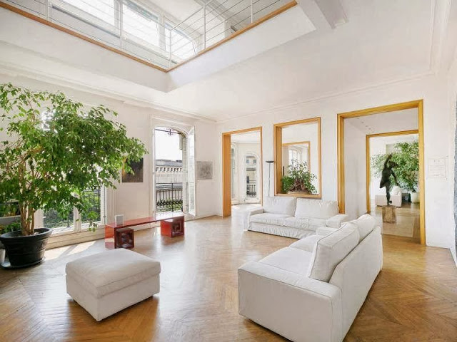 Living room in a Paris apartment with herringbone wood floor, white sofas and matching ottoman and a large potted plant
