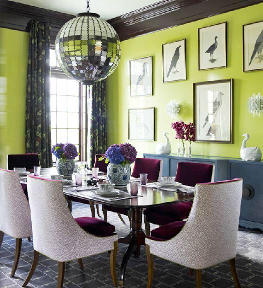 Alternative view of the dining room with apple green walls with framed prints of birds, purple chairs, a graphic grey and white rug, a disco ball pendant light, an encasement window with floor length patterned curtains and a blue-grey wall console
