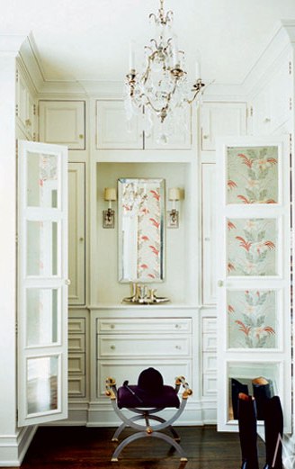 White dressing area with wood floor, crystal chandelier and mirrored doors reflecting floral curtains