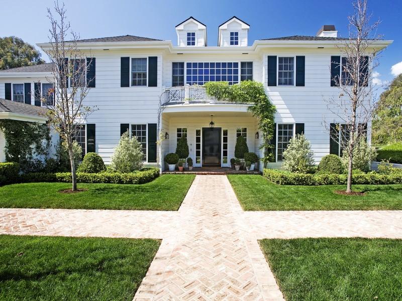 Front of white colonial style home in the Pacific Palisades with a lawn and herringbone brick walkway 