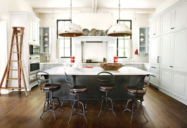 Kitchen with a large island that blends in with the dark wood floors, worn metal over sized pendant lights, white cabinets, and stainless appliances