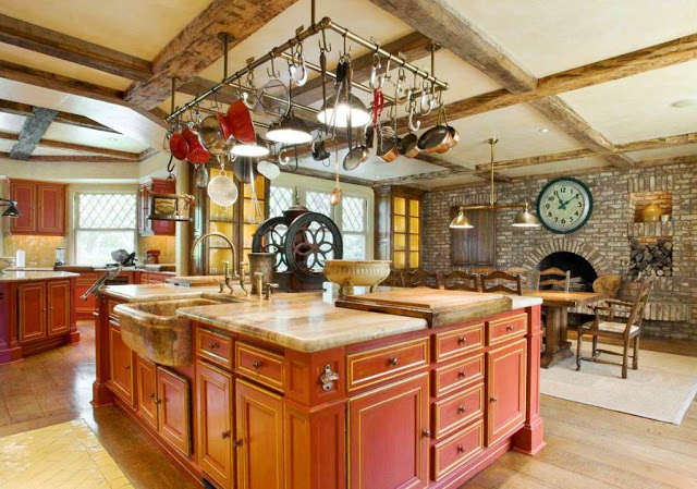 rustic, eat in kitchen in a mansion with red island, cabinets, stone fireplace, antique coffee grinder, hanging pot racks and visible beams