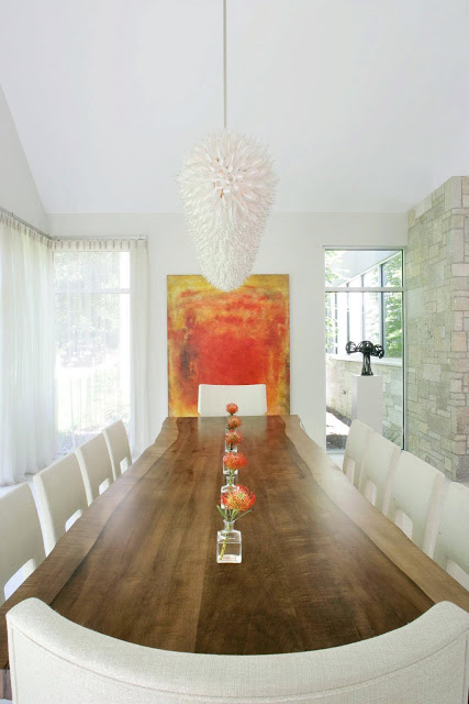 dining room in a modern farmhouse with white chandelier, long wood table, white chairs, large windows and a red and yellow piece of modern art on the wall