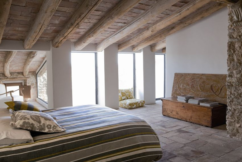 Loft bedroom with wood ceiling, exposed beams, a stone wall nook and simple furnishings