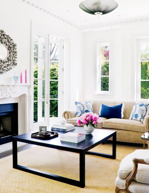 living room with French doors, a neutral sofa with blue accent pillows, a fireplace with molded mantel with a round mirror above it, a Louis XIV chair and a dark wood coffee table