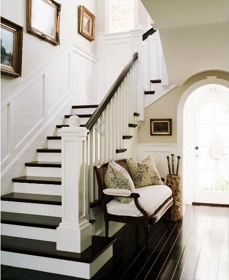 Foyer with dark wood Louis XVI bench with white cushions, dark wood floor and staircase