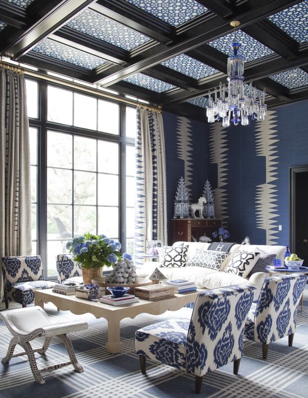 Blue living room with graphic print wall coverings and arm chairs, blue and white chandelier and patterned ceiling