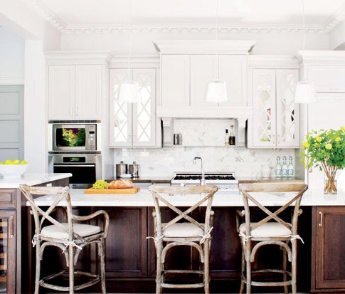 white kitchen with island with dark wood cabinets, reclaimed wood chairs and stone backsplash