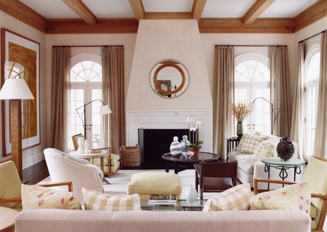 Living room with exposed beams, a white fireplace with a polished round mirror on the mantel, french doors and gingham accent pillows