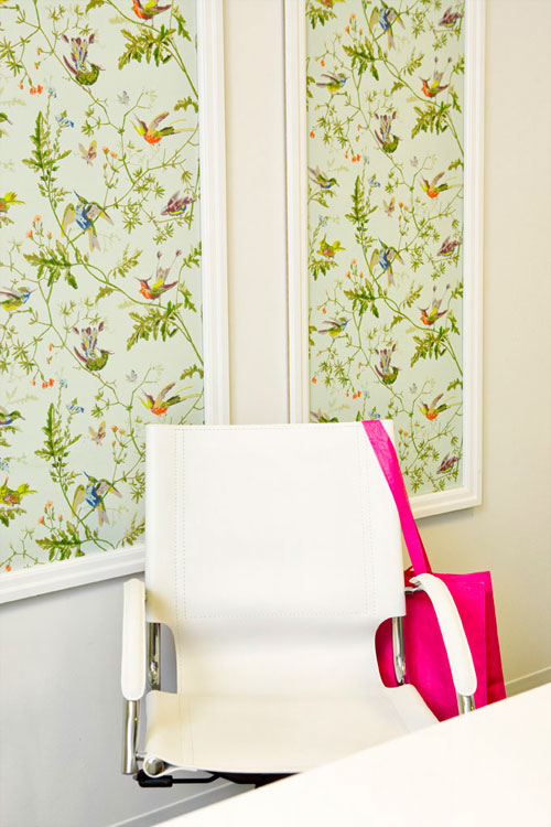 Office with framed light blue print with birds and foliage, a white chair and a hot pink purse