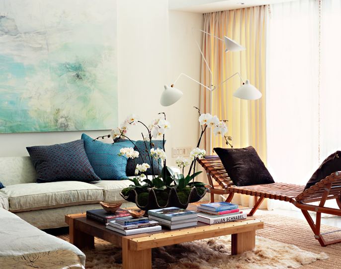 Living room with an L shaped sofa, a wood and leather strapped bench, a large over sized square wood coffee table and a white floor lamp with three lights bent in different directions