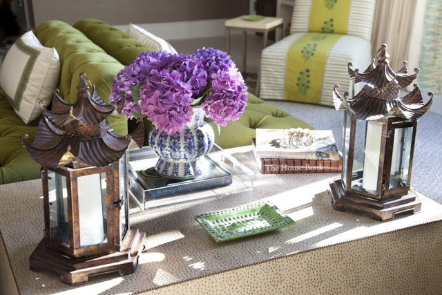  vignette in a living room featuring a textured coffee table with nail head trim, Chinoiserie accents in the form of lanterns and blue and white urn holding purple hydrangeas and a Lucite tra