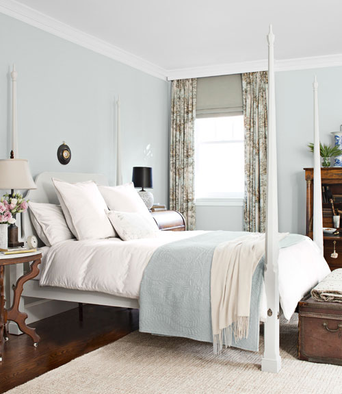 light blue and white bedroom with a four poster bed, floral curtains, a trunk at the foot of the bed, wood floor and a sisal rug