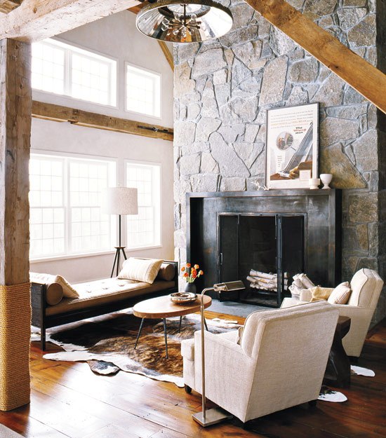 Living room with hide rug, club chairs, fireplace with a steel mantel and flagstone chimney and a bench with a light brown cushion and matching accent pillows