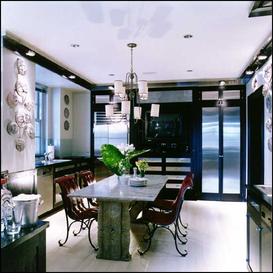 Eat in kitchen with black cabinets with stainless doors, white walls and tiled floor, a stone table with marble tabletop is surrounded by red leather upholstered chairs with wire legs. 