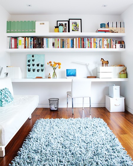 Floating wall length shelves in a home office with hardwood floor, a light blue shag rug and a white sofa
