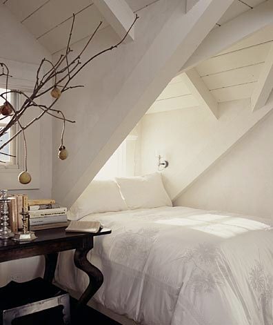 white attic bedroom with exposed beams and a dark wood side table