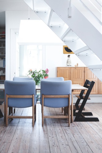Dining room in a Danish home with blue chairs and stained wood cabinets