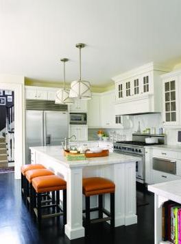 Kitchen with darkwood floor, white drawers and cabinets, stainless appliances, two pendant lights, an island with a marble countertop and white base surrounded by orange counter stools