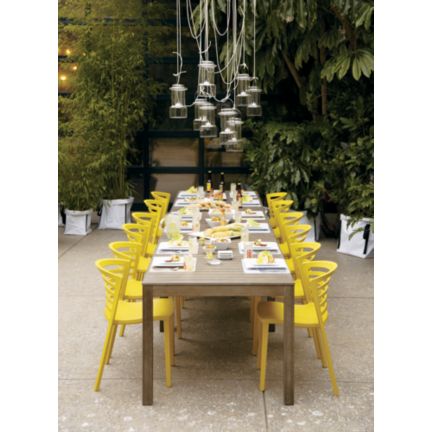 Outdoor dining set up with a long wood table, Venezia Mustard Yellow Chairs, lanterns and lots of bamboo and other plants