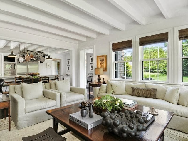 Open plan living room of a house on an East Hampton compound with grey sofas and armchair and beamed ceiling