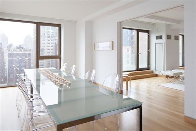 New York City penthouse dining room with ghost chairs, a glass top table, light wood floors, and a great view of the city