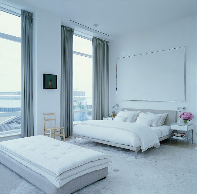 modern grey and white bedroom with upholstered headboard, large windows with floor length curtains and a long ottoman