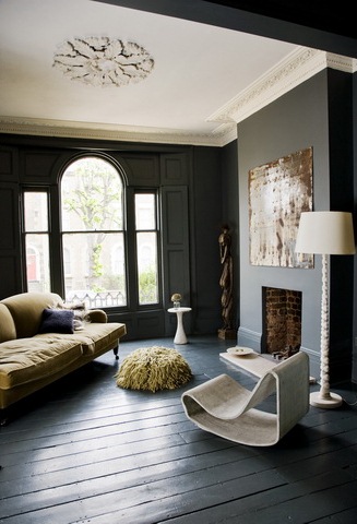 Black living room with white ceiling moulding, dark wood floors, arched windows, a green sofa, a simple fireplace and a modern sea grass chair
