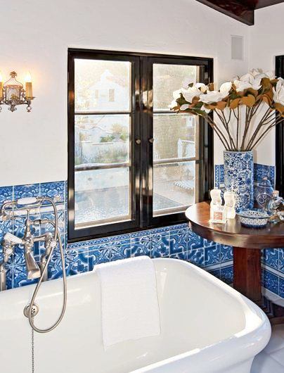 close up of blue and white bathroom tiles near black framed windows, stand alone bathtub and small round accent table