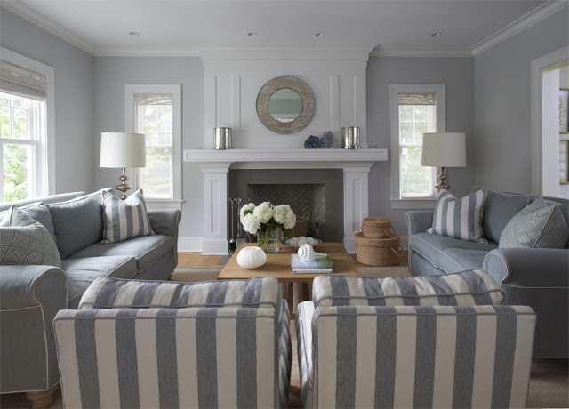 Grey living room with grey dueling sofas, a white molded fireplace, a wood coffee table and two blue and white striped armchairs