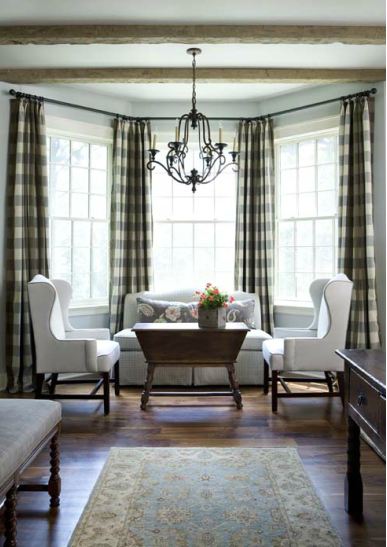 Living room with gingham curtains, white dueling armchairs, a rustic coffee table and chandelier 