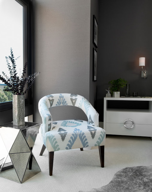 Close up of an upholstered chair with a mirrored side table in a grey bedroom