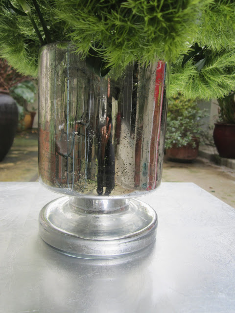 Close up of mercury glass cylinder vase on a metal table on a patio