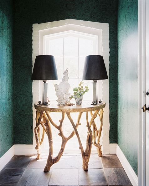Malachite wallpaper in Kristi Bender's foyer with an organic circle table, parrot statues and two matching lamps with black shades