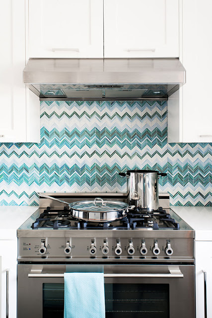 close up in blue and white zig zag chevron tiles, white cabinets and polished metal stove in a kitchen by Jute